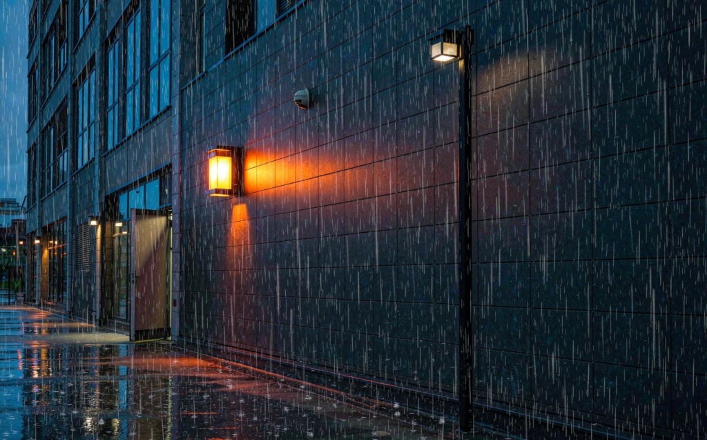 Rain-lit street at blue hour with warm light pools from sealed IP65 outdoor light fixtures on poles and walls
