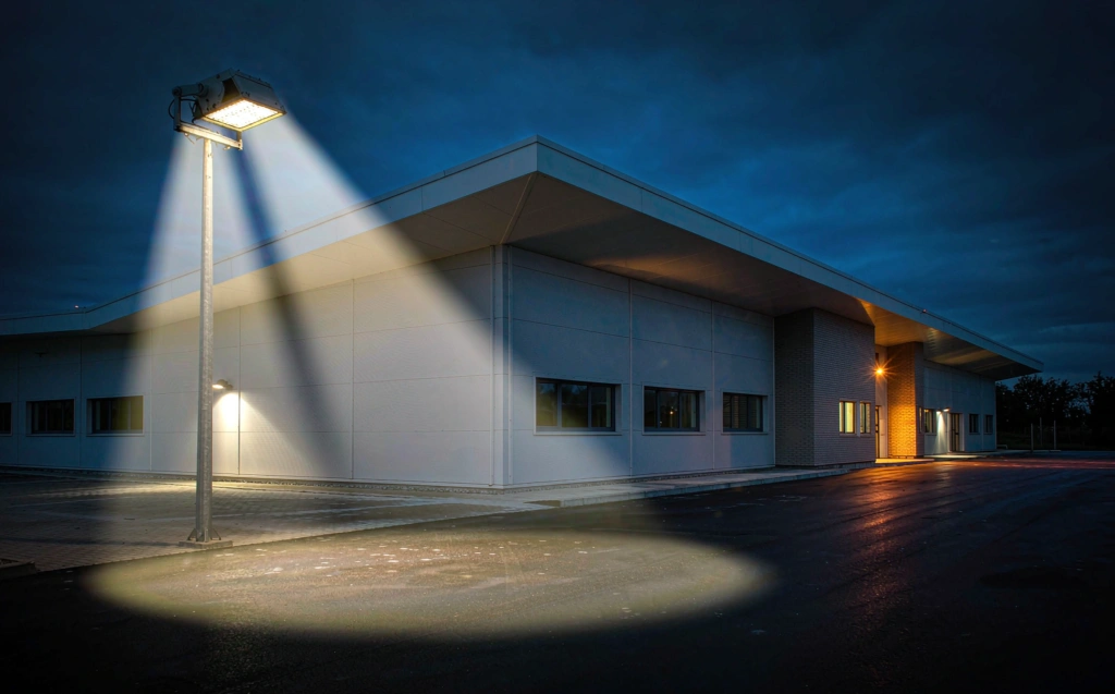 Photorealistic dusk scene of LED flood lights illuminating a warehouse parking area